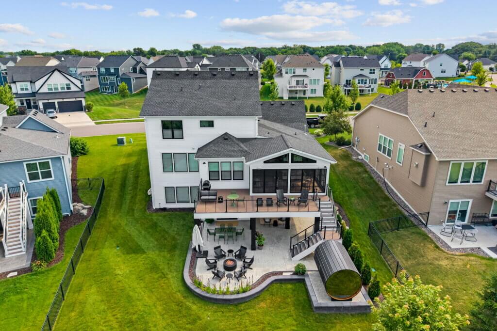 Aerial view of a completed elevated deck and three-season porch with stairs, patio, fire pit, and barrel sauna.