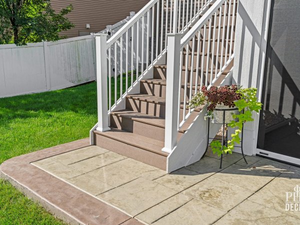 The Oakview Deck stairs with Dark Oak treads, white railing, stamped concrete patio, and retractable screen.